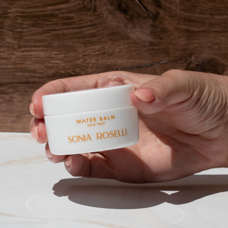 Hand holding a white container of Sonia Roselli water balm against a wooden background