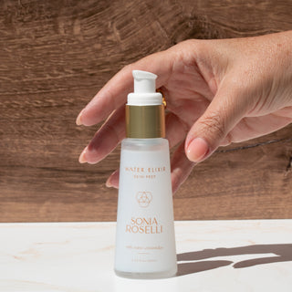 Hand holding a bottle of Sonia Roselli Water Elixir against a wooden background