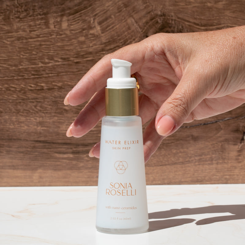 Hand holding a bottle of Sonia Roselli Water Elixir against a wooden background