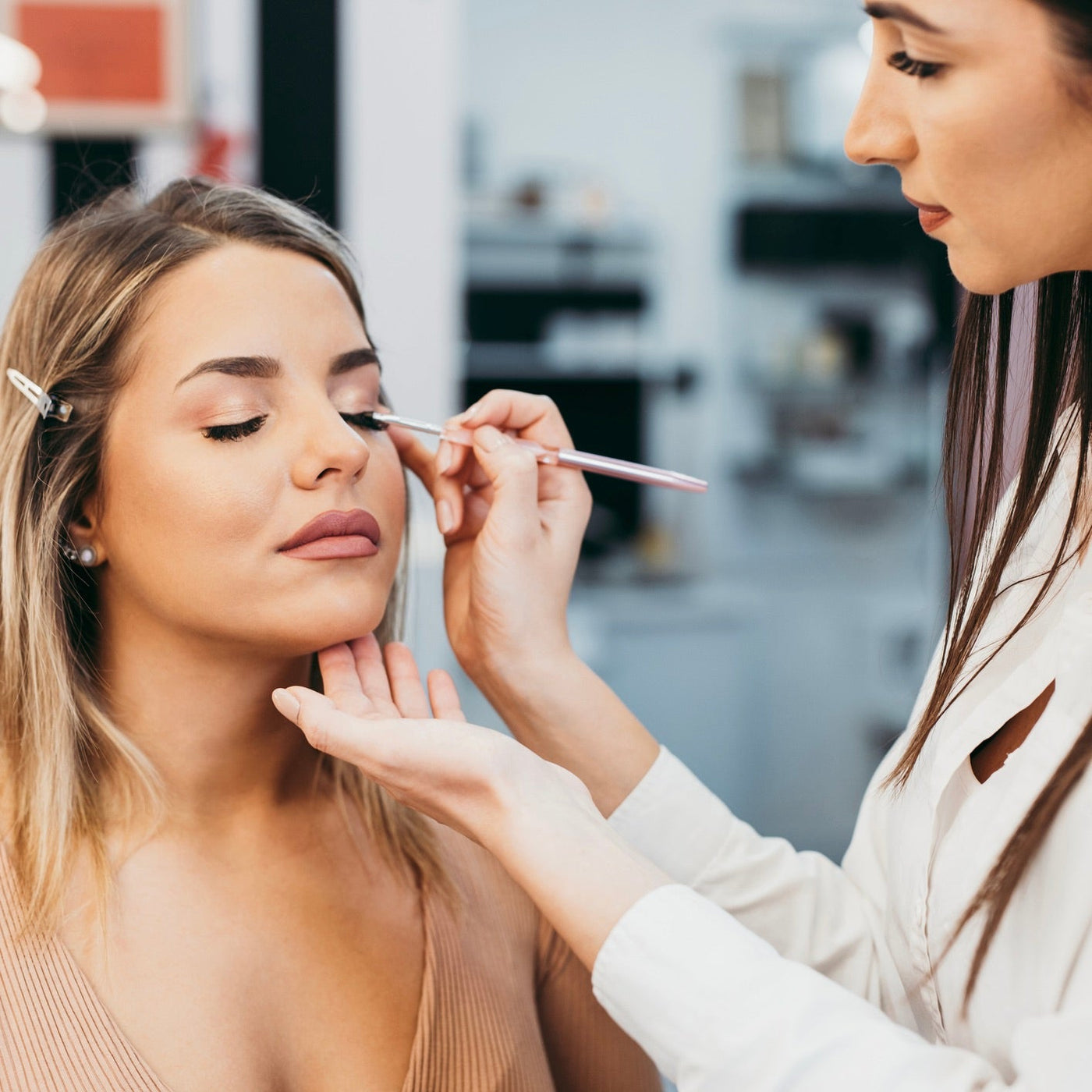Makeup artist applying eye makeup to woman using a brush.